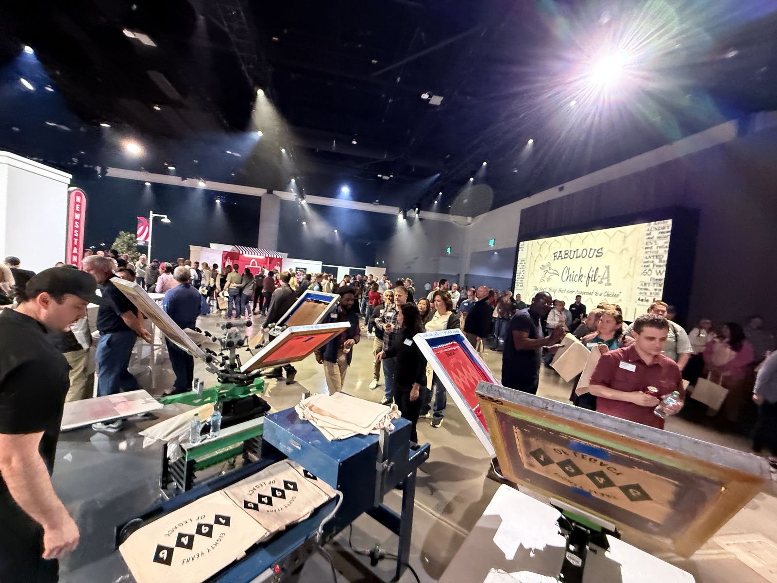 Busy convention hall with a crowd gathered around live customization stations under stage lighting