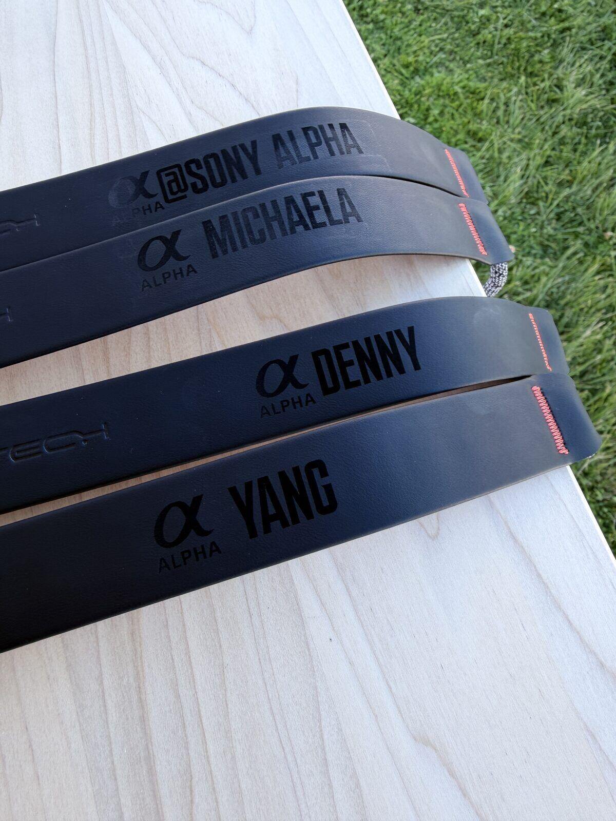 Stack of black camera straps each laser-engraved with a different guest name at a brand activation