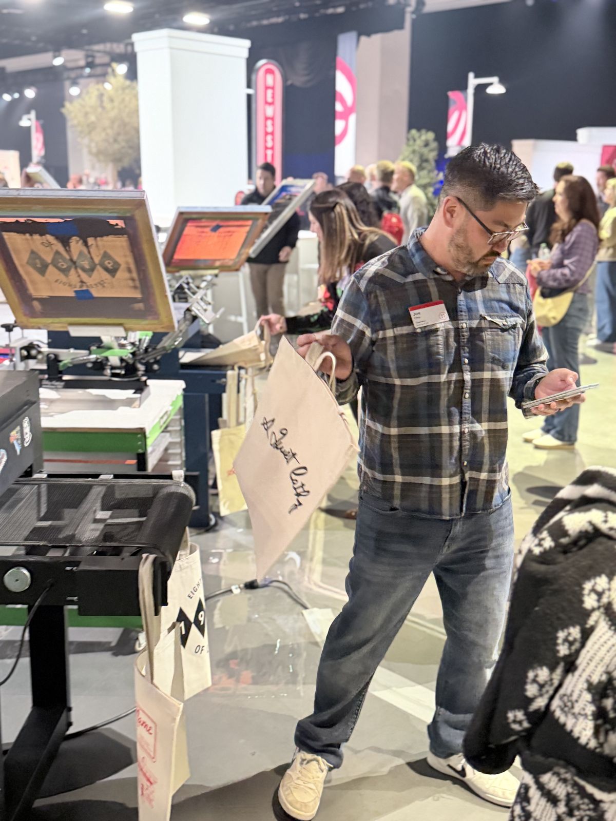 Attendee with a customized tote beside press equipment on an expo floor